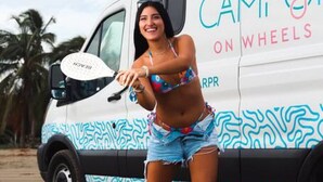 Una persona in bikini in piedi di fronte a un furgone bianco con scritte e illustrazioni colorate.