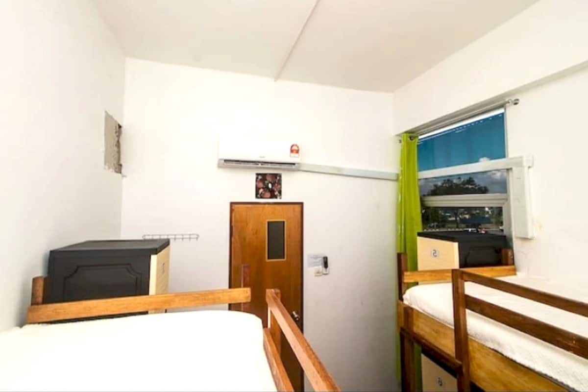 Quarto pequeno e compacto com duas camas beliche, uma porta de madeira e janela com vista para o exterior.