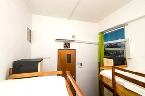 Een kleine, compacte kamer met twee stapelbedden, een houten deur en een raam met uitzicht op buiten.
