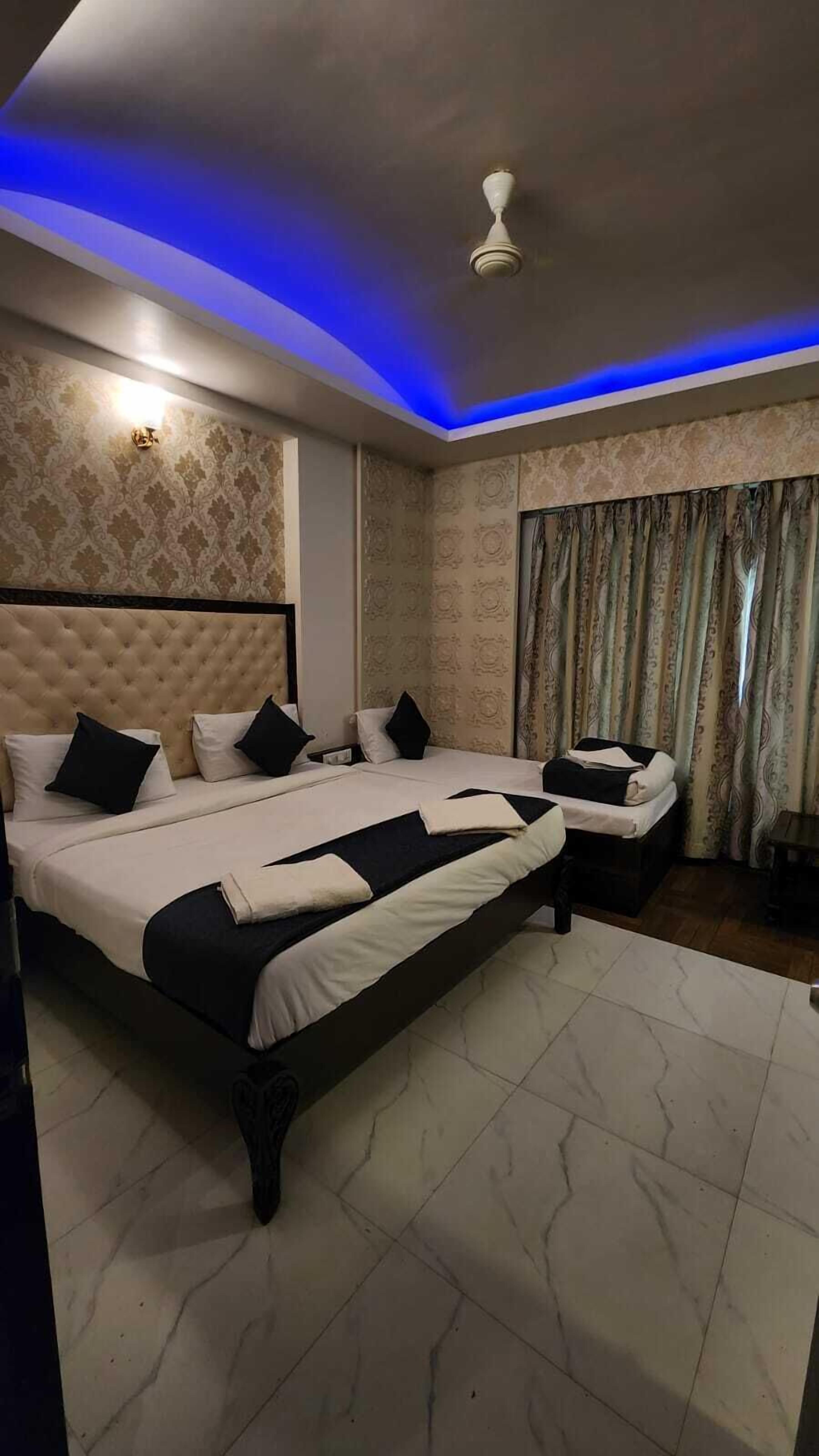 Habitación de hotel con una cama grande, dos mesitas de noche, un ventilador de techo y papel tapiz estampado.
