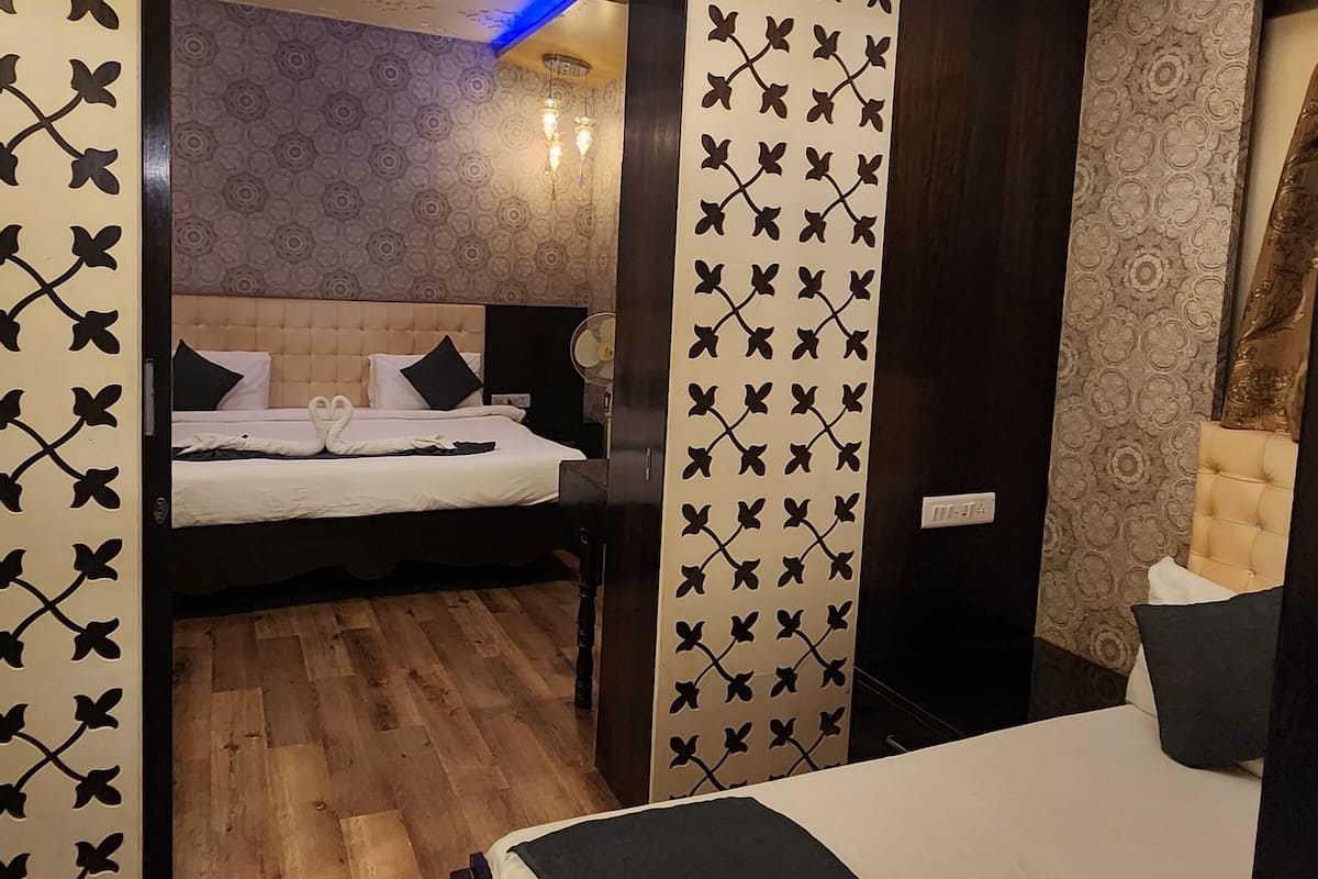 A hotel room with a large bed, a smaller bed in the background, a chandelier, and a wooden floor.
