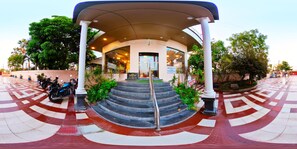 A hotel entrance with a covered staircase, palm trees, and a tiled floor.