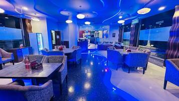 Interior moderno de restaurante con iluminación azul, mesas y sillas redondas.