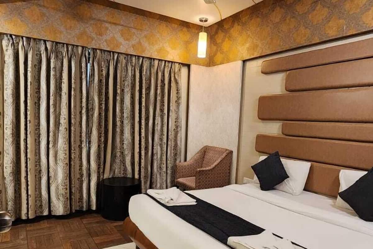 A hotel room with a large bed, a ceiling fan, patterned curtains, and a wooden headboard.