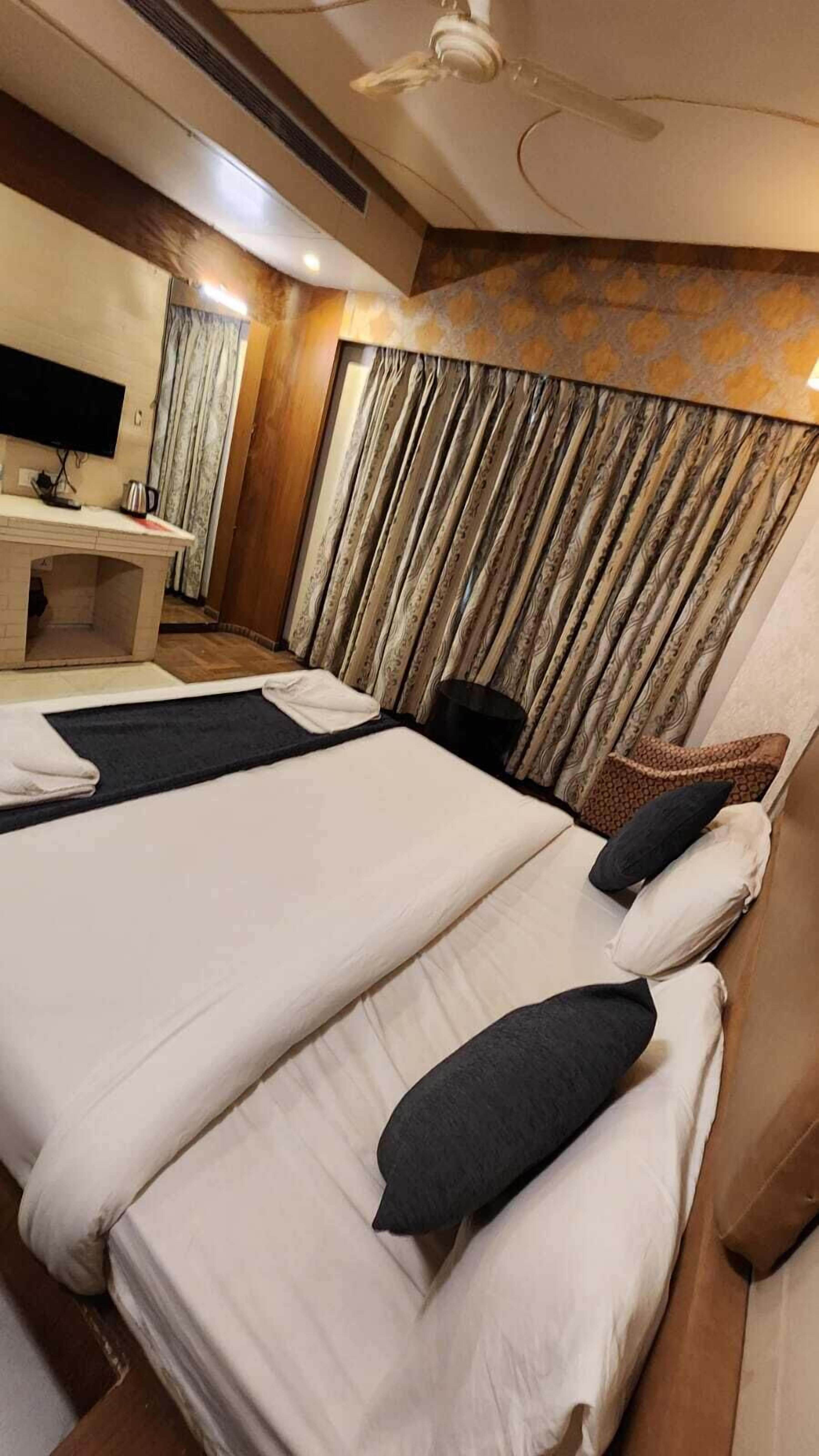 Habitación de hotel con dos camas, un escritorio y un televisor de pantalla plana, además de un ventilador de techo.