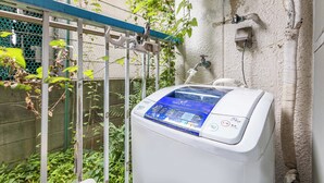 A white washing machine with a digital control panel, a metal rack, and a water outlet on a wall. - Esterrace Osaka West (Osaka)