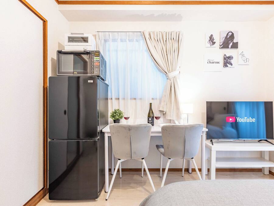 Habitació d'hotel senzilla amb cuineta, menjador amb dues cadires, televisió que mostra YouTube i un llit.