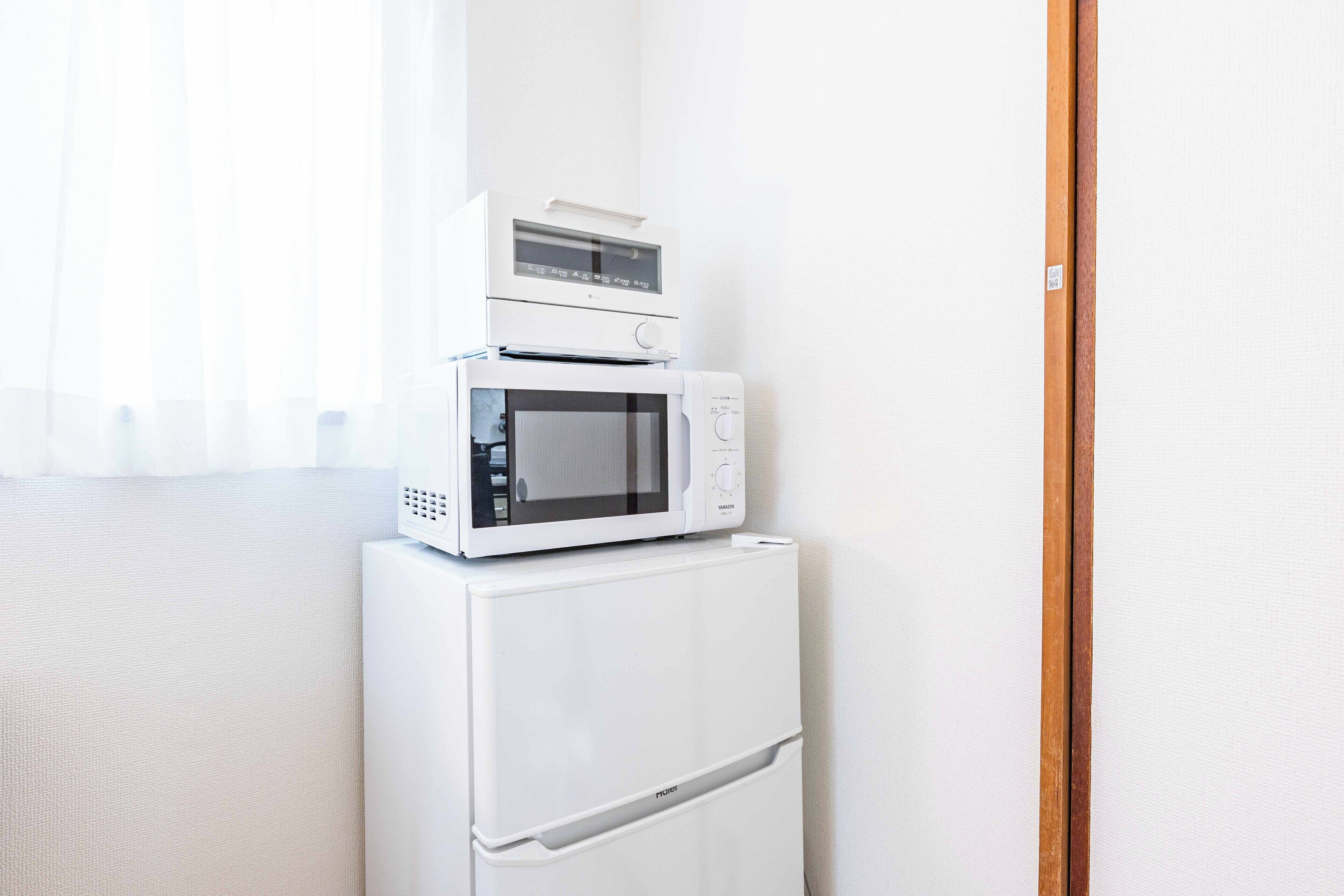 Een witte koelkast met een magnetron erboven, een houten deurkozijn en een witte muur.
