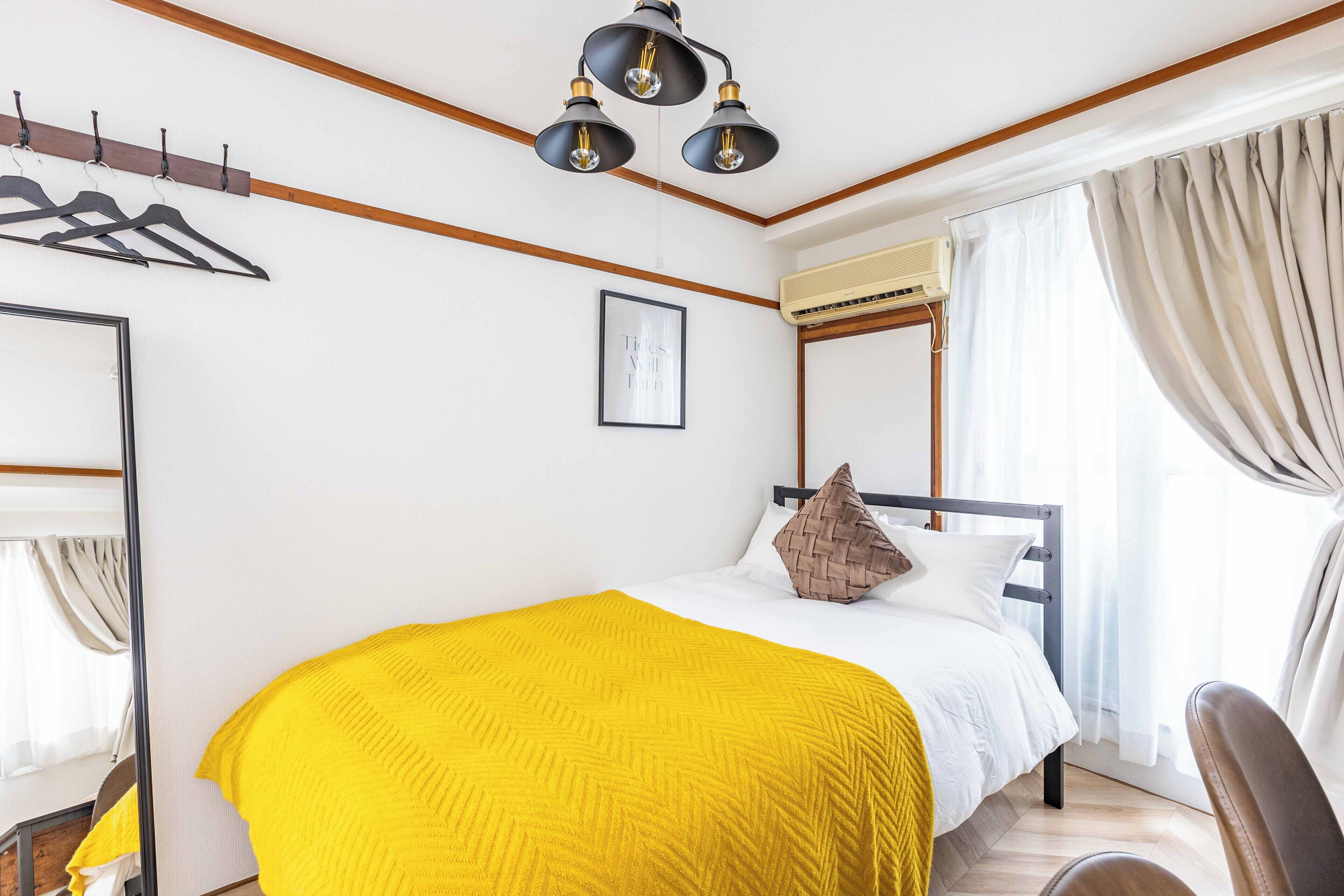 A bedroom with a bed, a hanging light fixture, a framed picture, and a window with curtains.