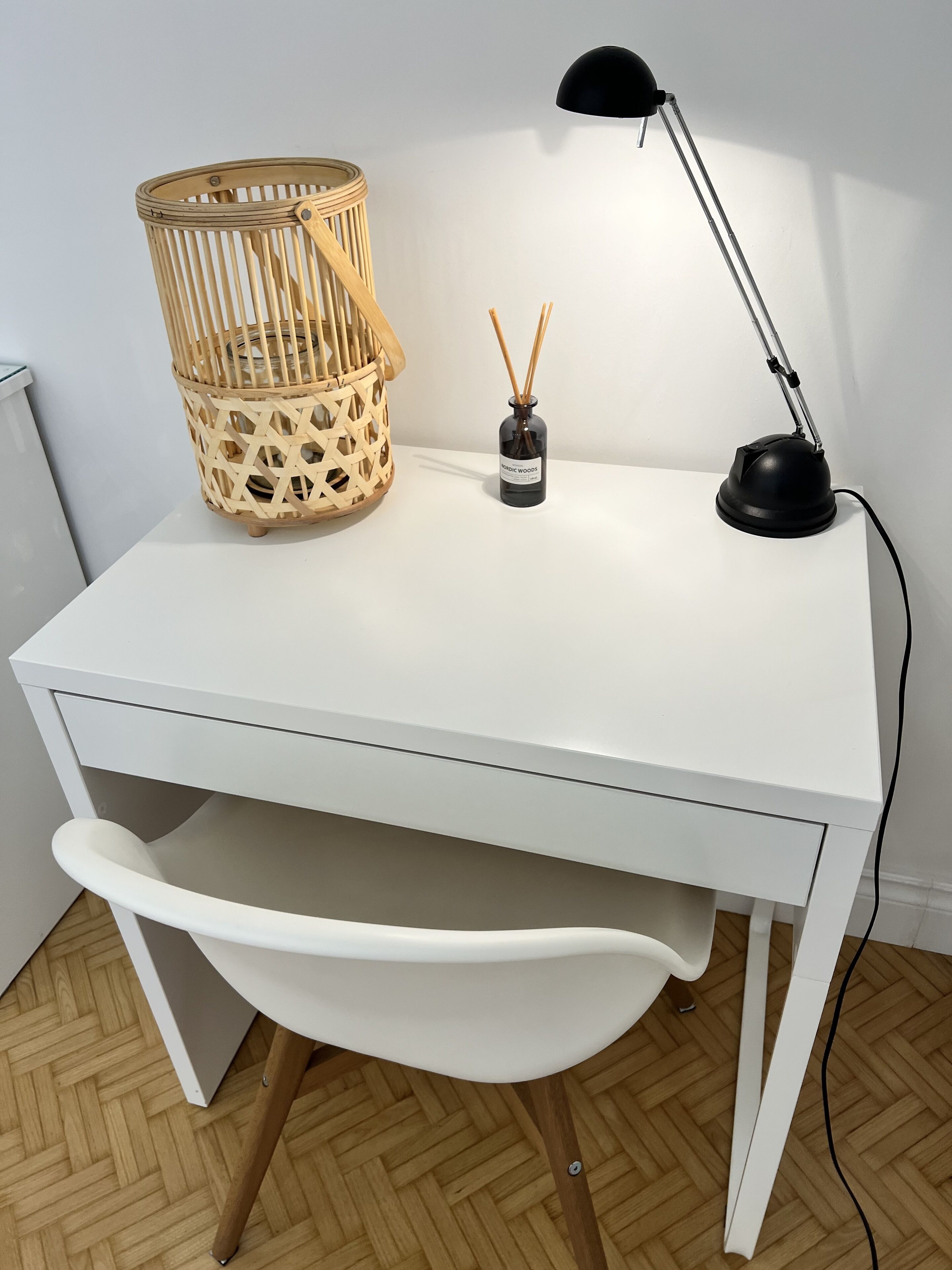 A white desk with a woven basket, a desk lamp, and reed diffusers.