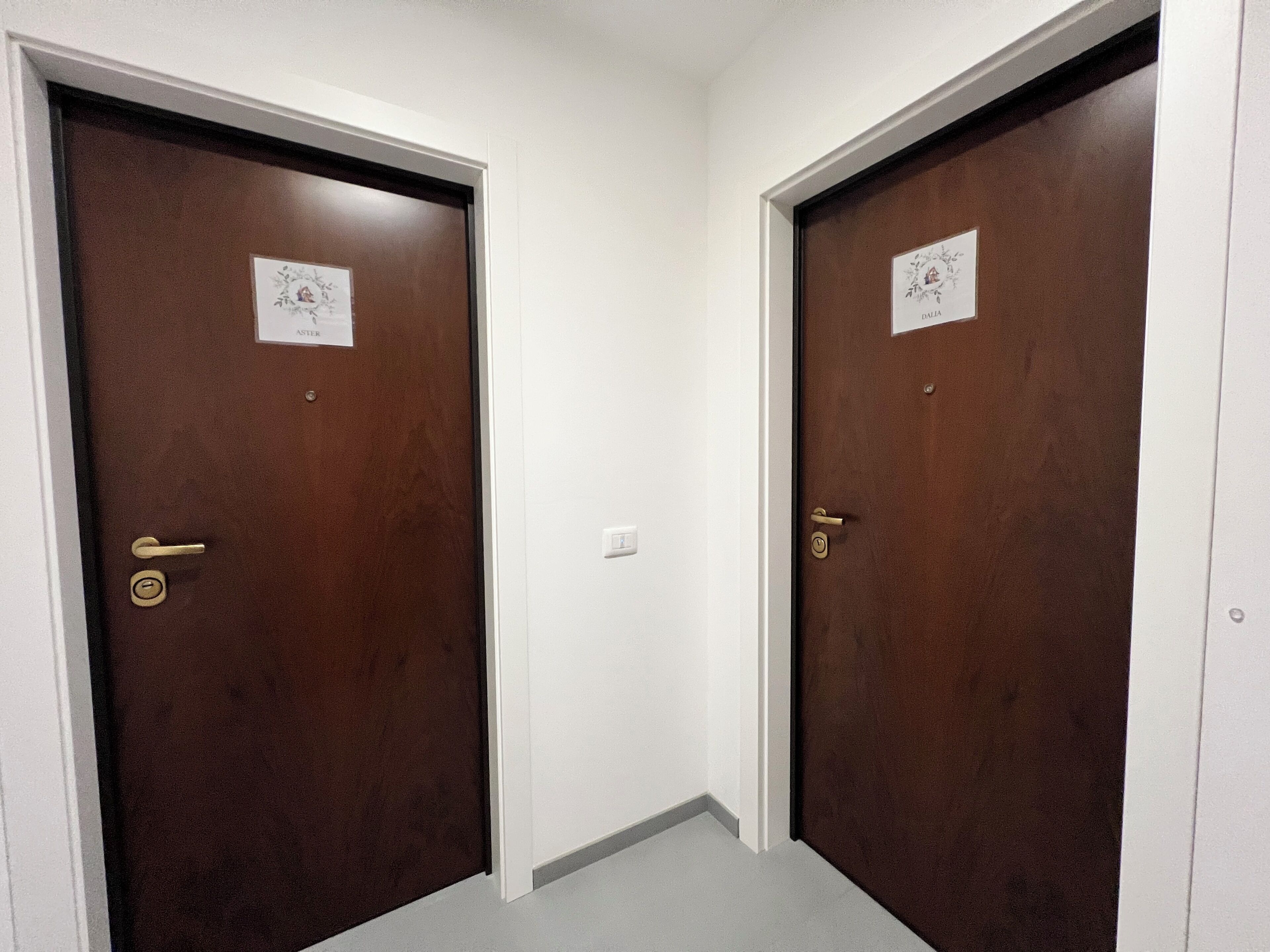 Zwei braune Türen mit weißem Rahmen, einem Lichtschalter und jeweils einem kleinen Schild.