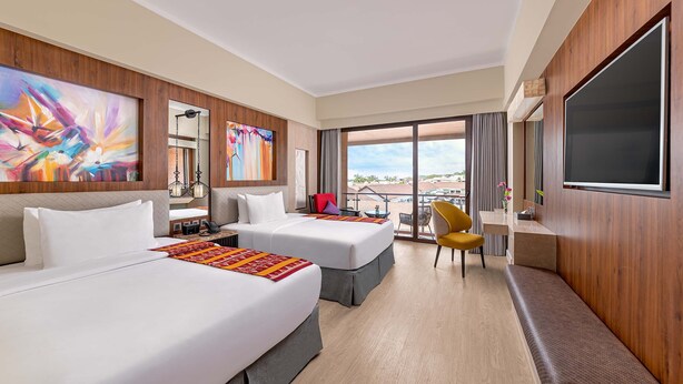 Habitación de hotel con dos camas, un escritorio, una silla, un televisor y ventanas amplias con vistas.