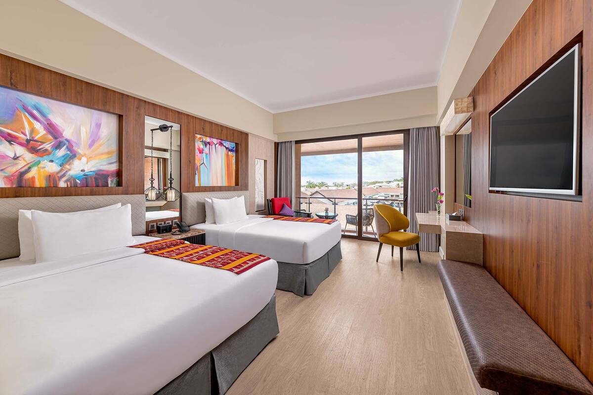 Habitación de hotel con dos camas, un escritorio, una silla, un televisor y ventanas amplias con vistas.
