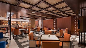 A modern restaurant with a checkered floor, wooden ceiling, and orange chairs.
