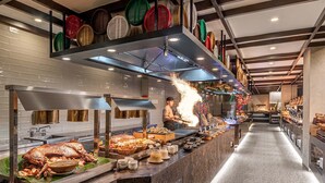 Montaje de bufé con un pollo asado como pieza central, diversos acompañamientos y un chef preparando comida.