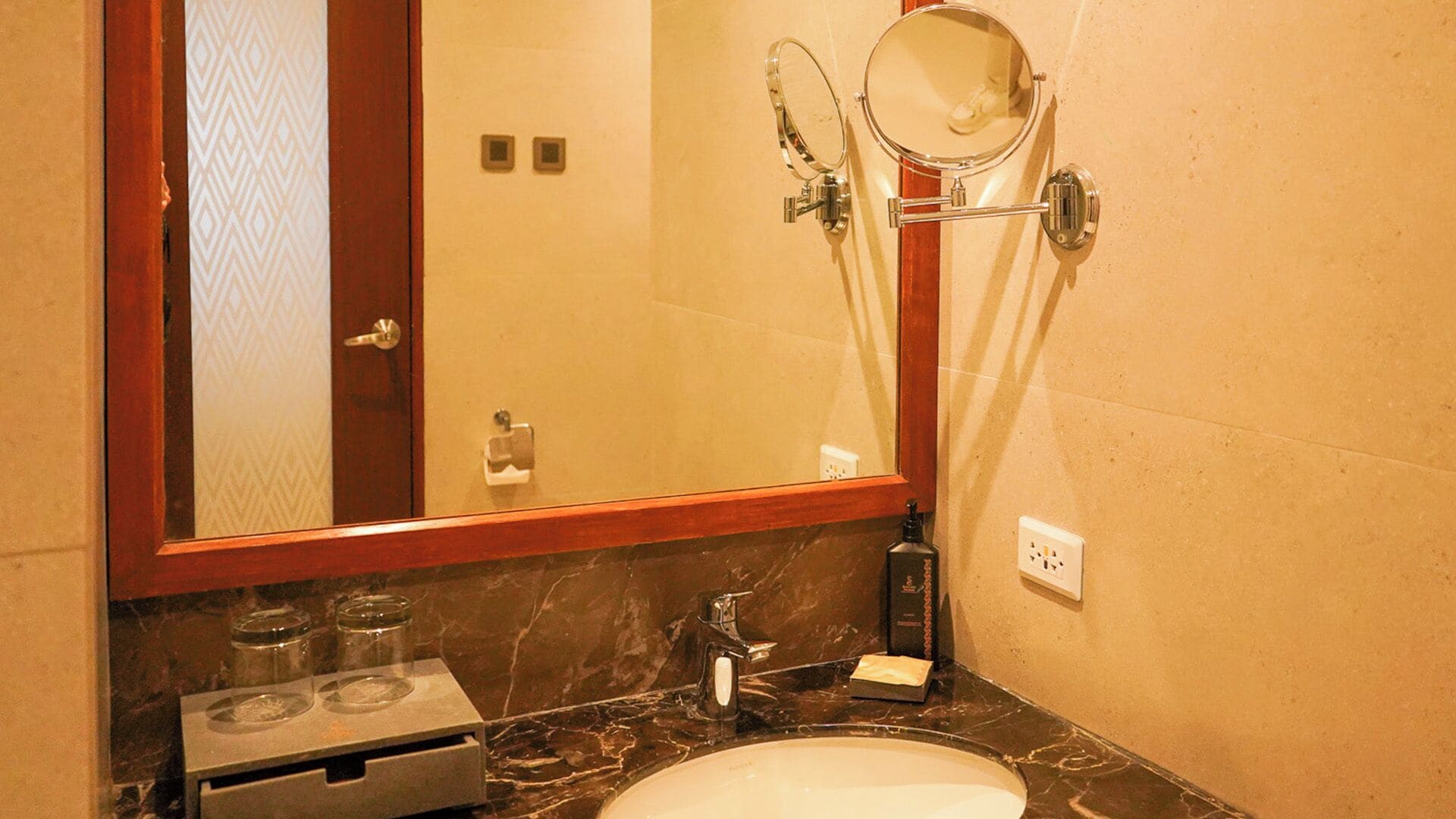 A bathroom with a marble sink, a mirror, a towel rack, and a towel dispenser.