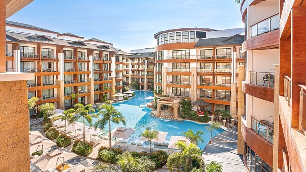 Un hotel con varios pisos, una piscina central y zonas de estar al aire libre.