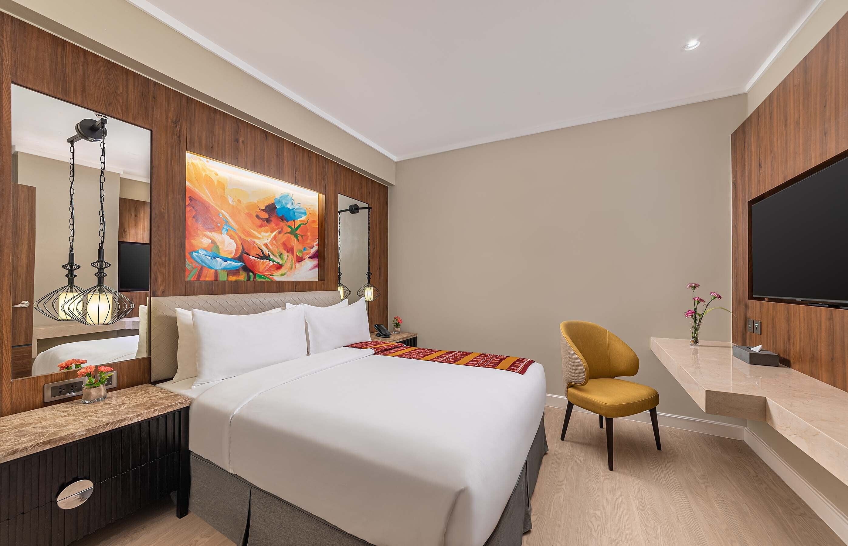 A modern hotel room with a large bed, a desk, a chair, a TV, and a painting on the wall.