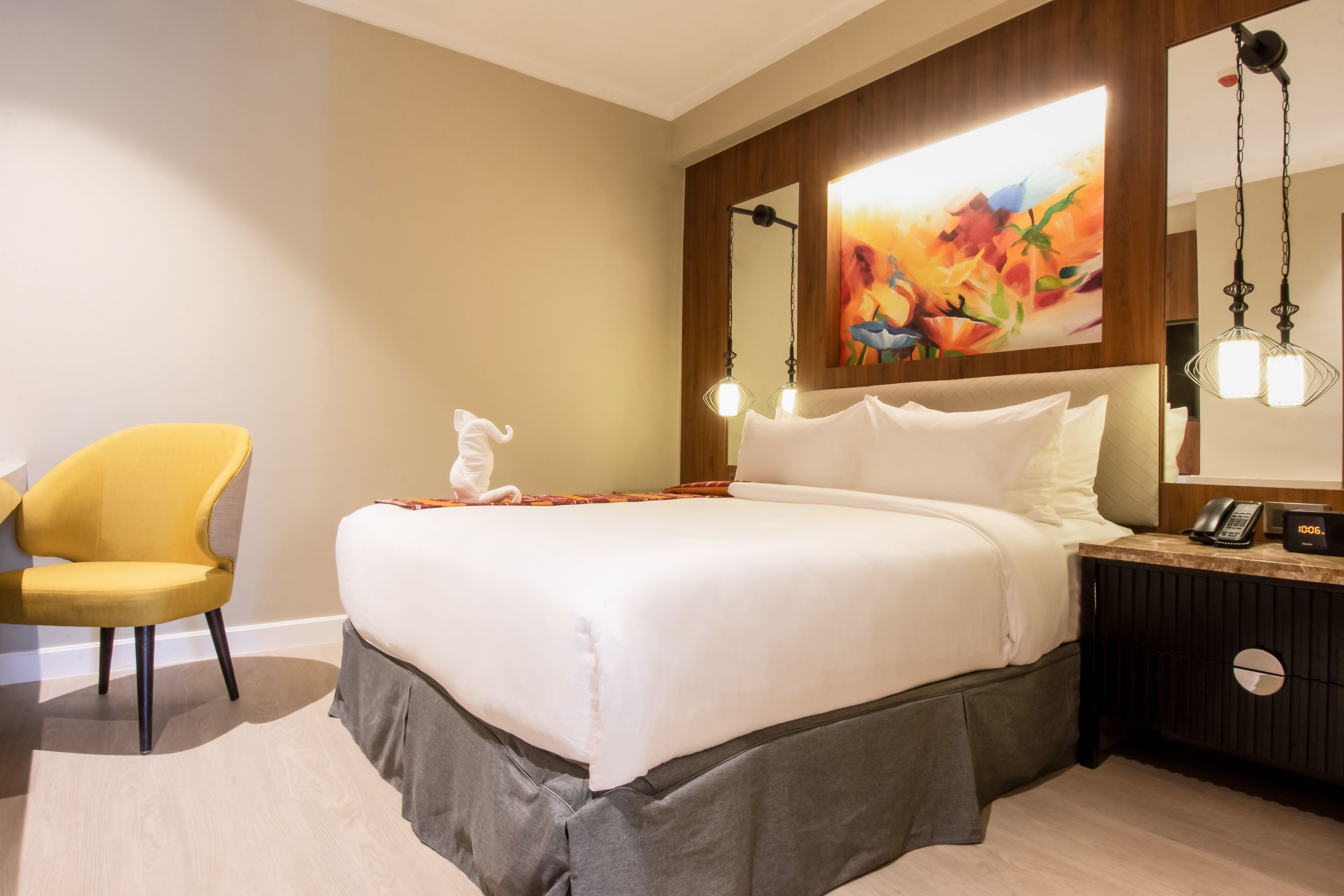 A hotel room with a large bed, a bedside table with a phone and a lamp, a chair, and a painting on the wall.