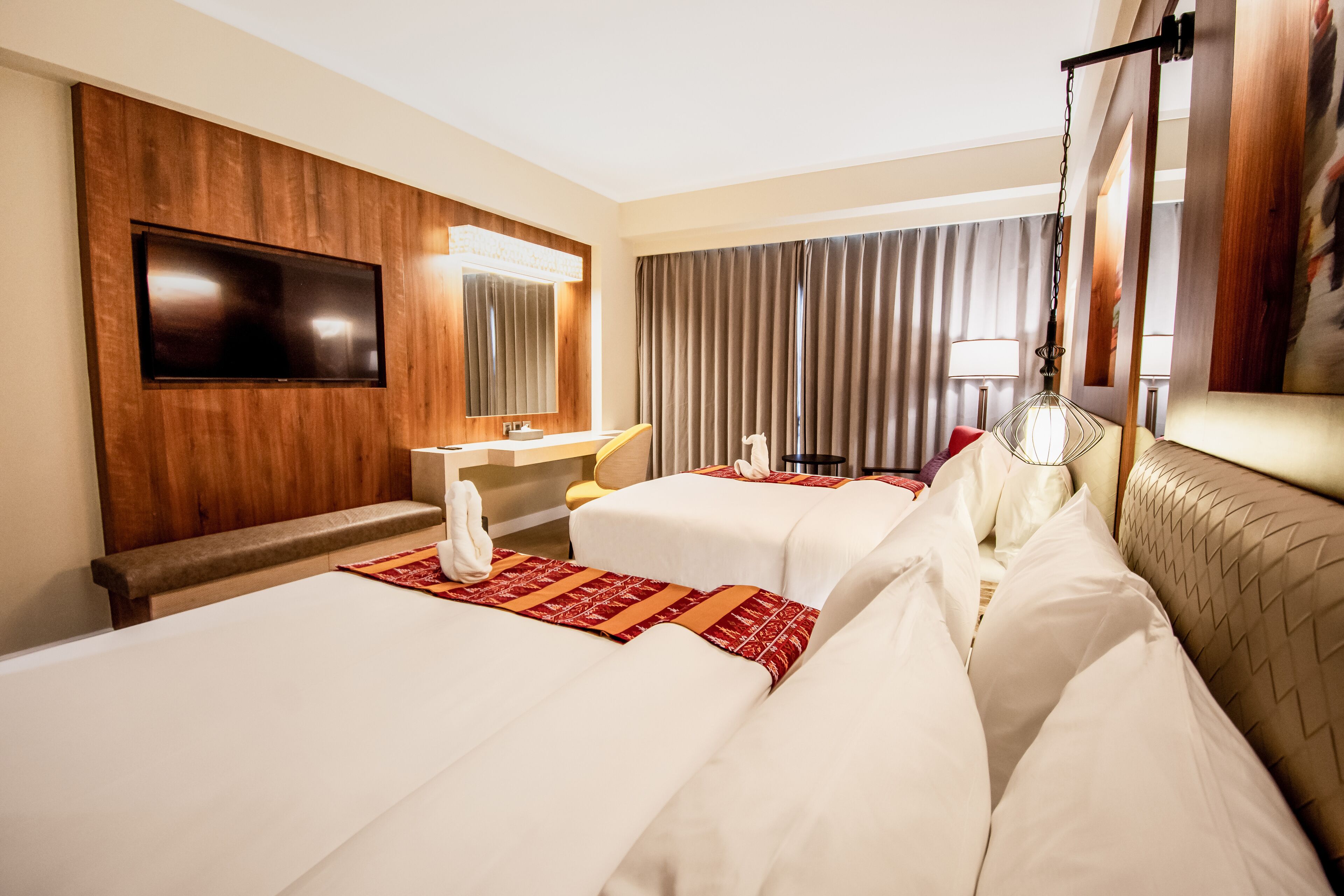 Habitación de hotel con dos camas, televisión, espejo, lavabo y un ventanal grande con cortinas.