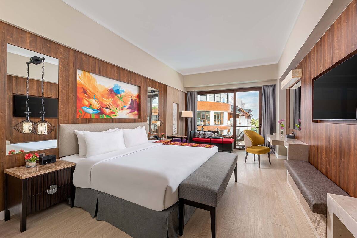 Habitación de hotel con una cama grande, un escritorio con lámpara, televisión y vistas al exterior.