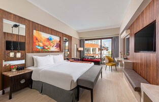 A hotel room with a large bed, a desk with a lamp, a TV, and a view of the outside.