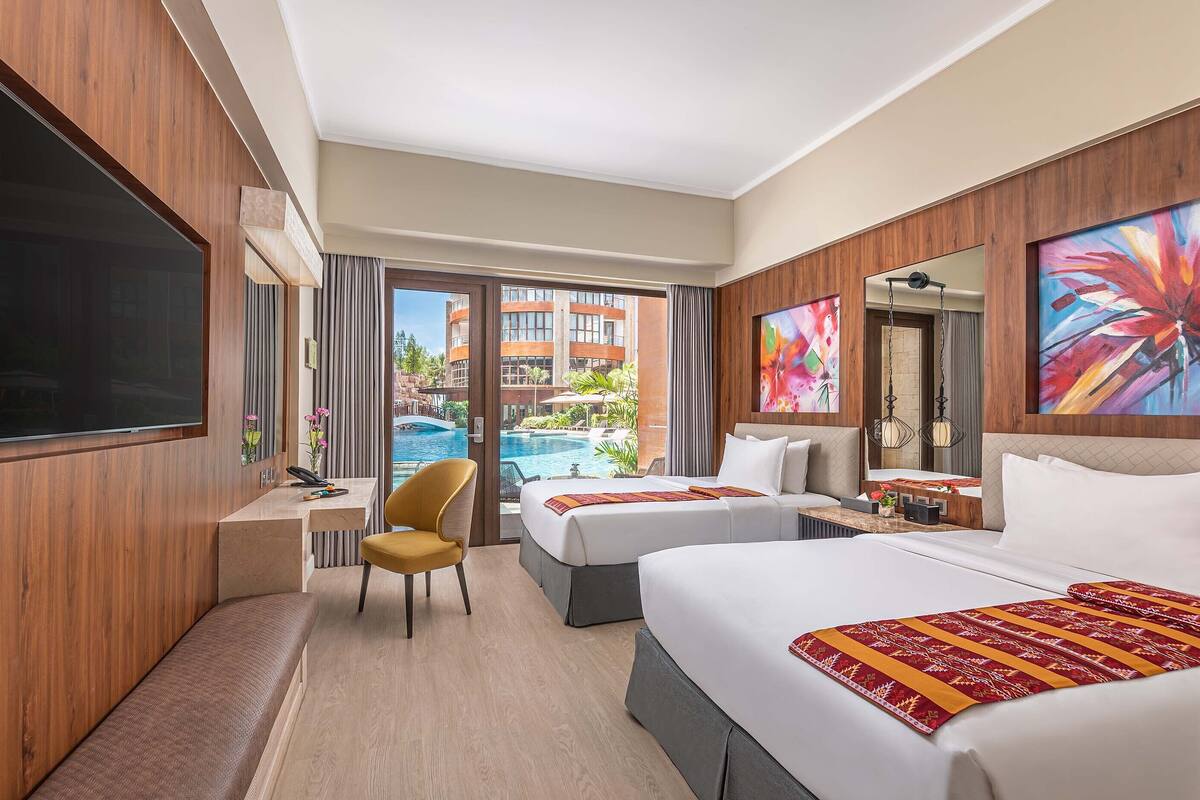Habitación de hotel con dos camas, un escritorio, una silla y un televisor grande.