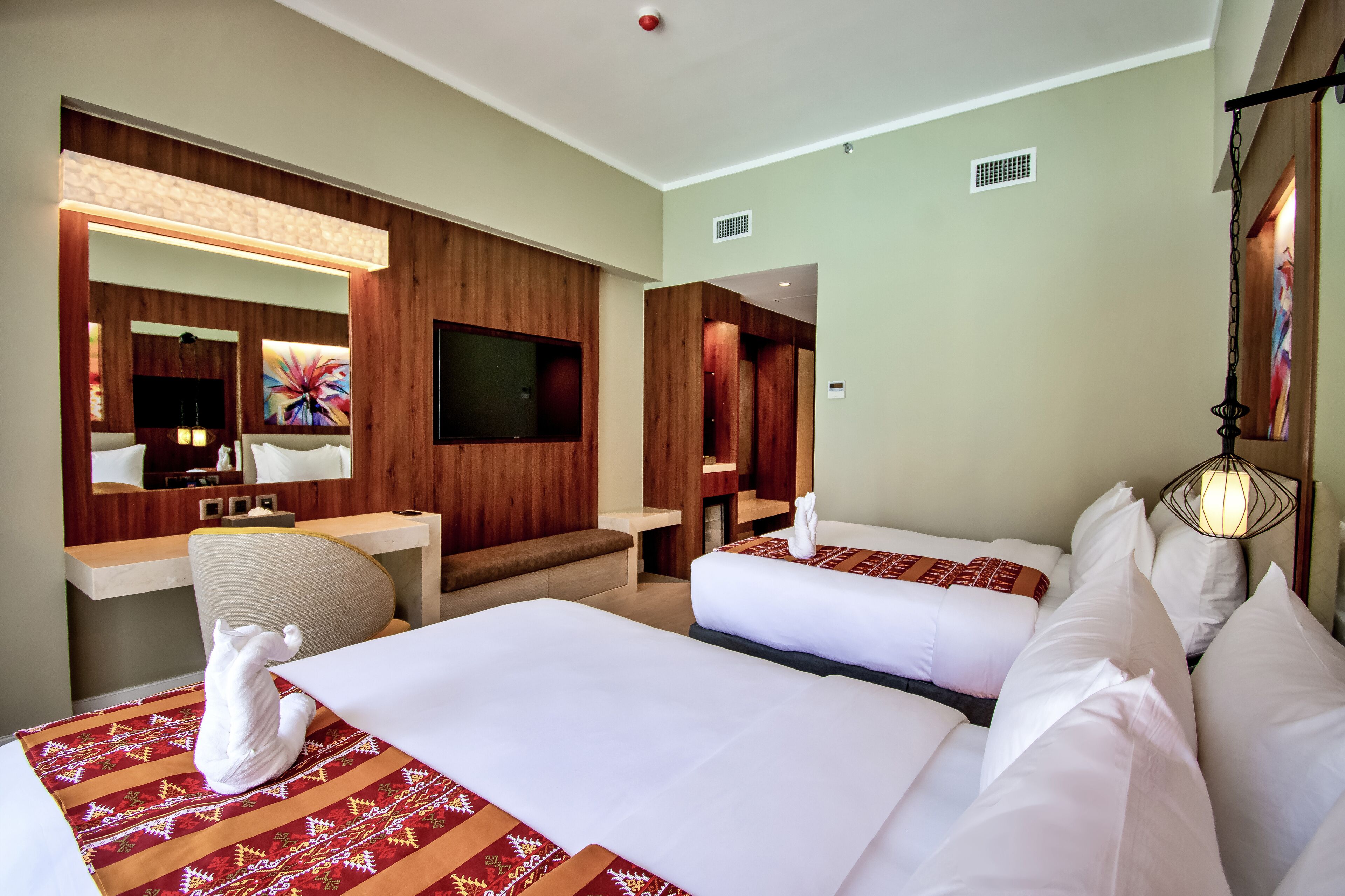 A hotel room with two beds, a sitting area, a TV, and a large mirror.