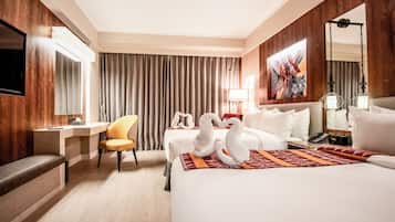 A hotel room with a bed, two bedside tables, a desk, a chair, a TV, and a large mirror.