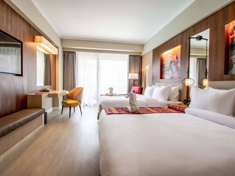 A hotel room with two beds, a desk, a chair, and a large window with curtains.
