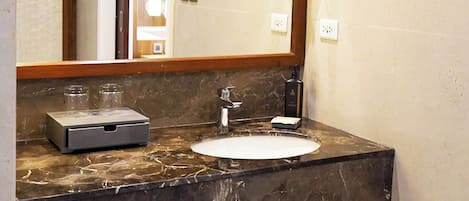 Un baño con encimera de mármol, lavamanos, espejo y toallero.