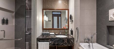 Un baño moderno con ducha de vidrio, tocador de mármol, espejo grande y bañera.