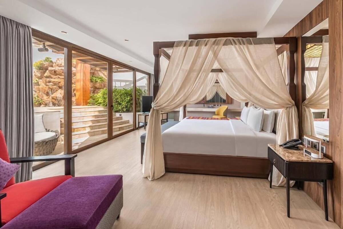 Un dormitorio moderno con una cama grande, un balcón con vistas a rocas y vegetación, y una silla roja.