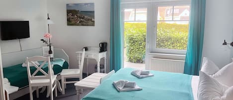A hotel room with a bed, a desk, a chair, a TV, and a window with curtains.