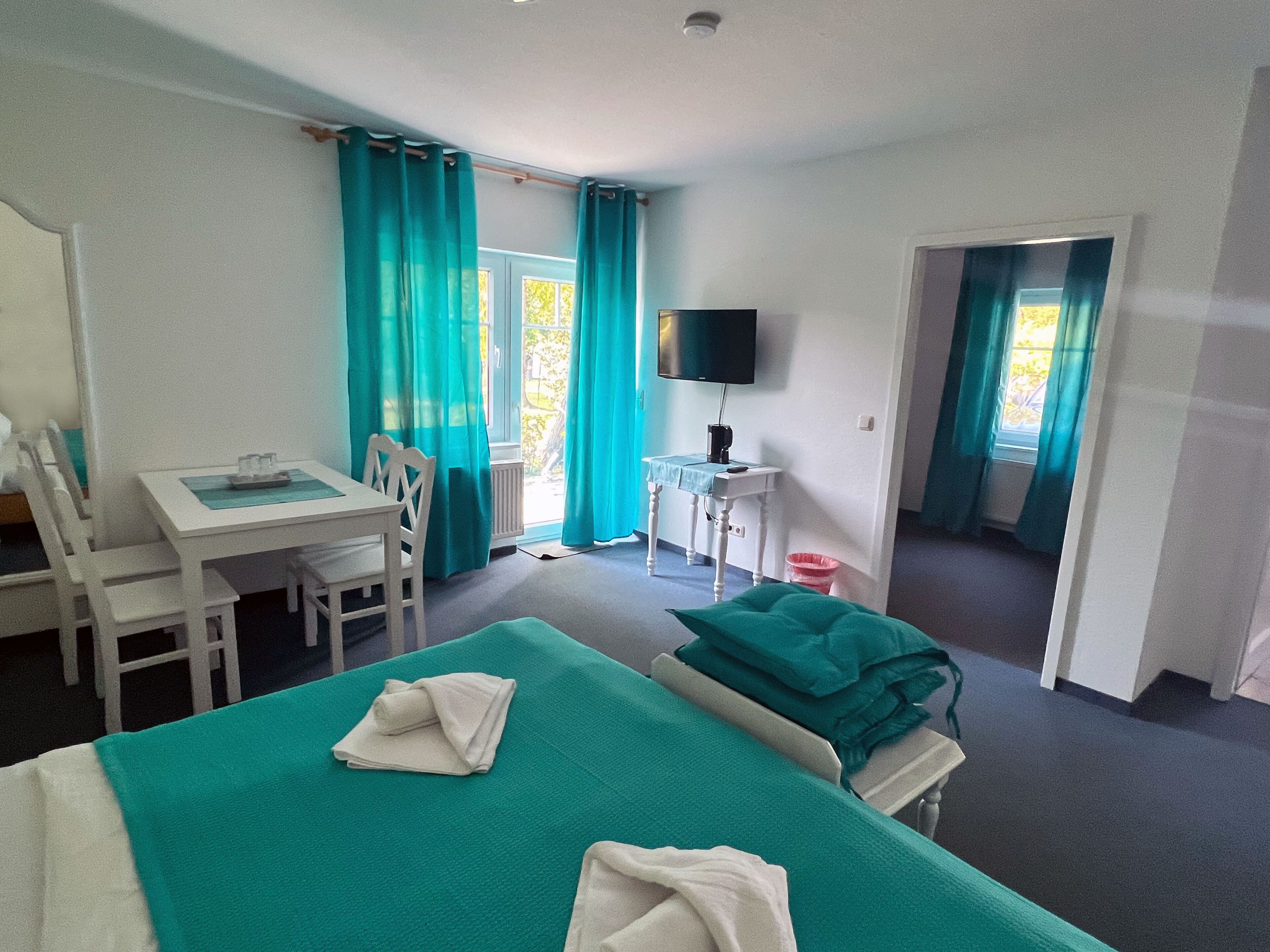 Habitación de hotel con cama, escritorio, silla, televisor y ventana con cortinas.