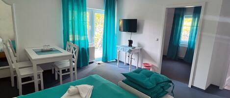 Habitación de hotel con cama, escritorio, silla, televisor y ventana con cortinas.