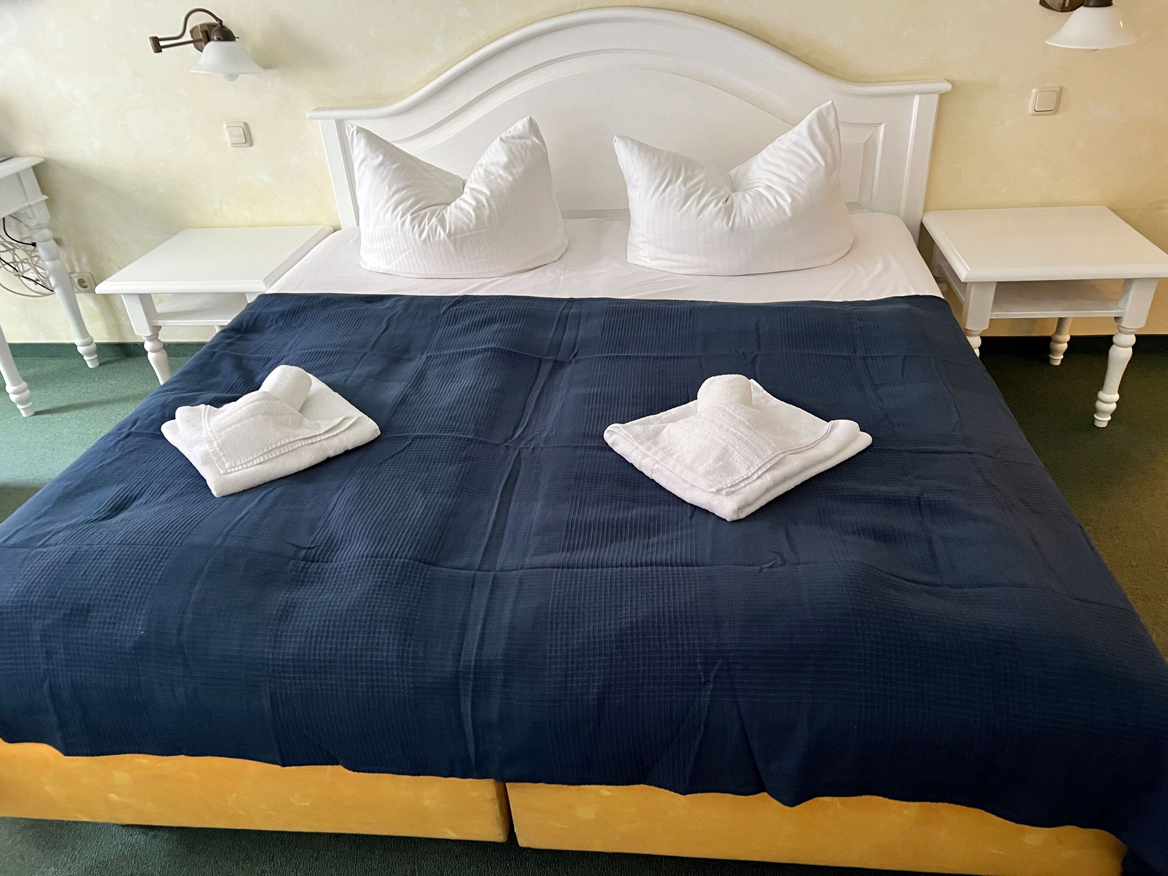A neatly made bed with a dark blue bedspread and two white towels folded on it.