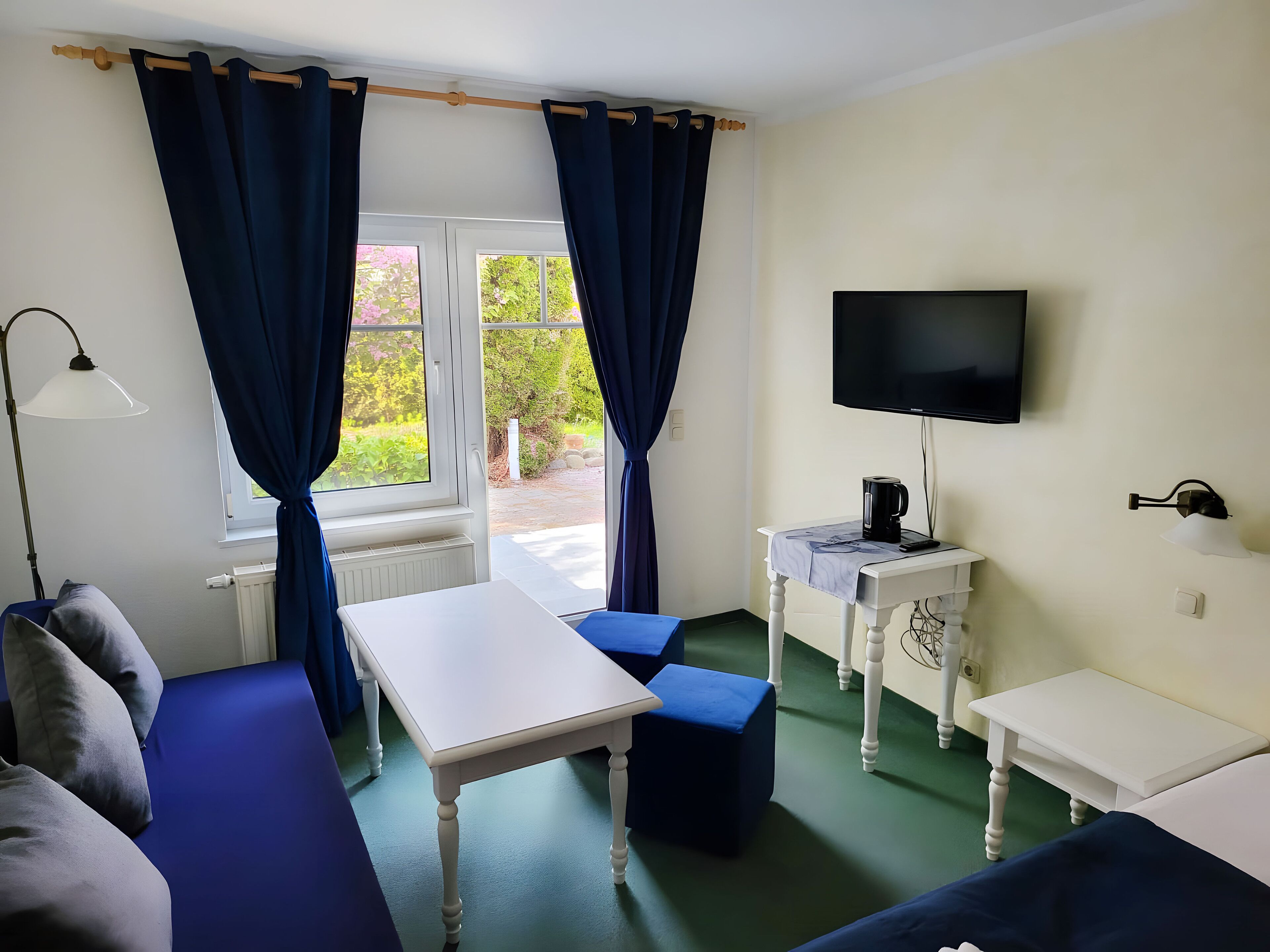 A room with a white table, blue chairs, a TV, a lamp, and a radiator.