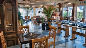 A spacious restaurant with wooden tables and chairs, large windows, and potted plants. - Hotel und Restaurant Windland (Breege)