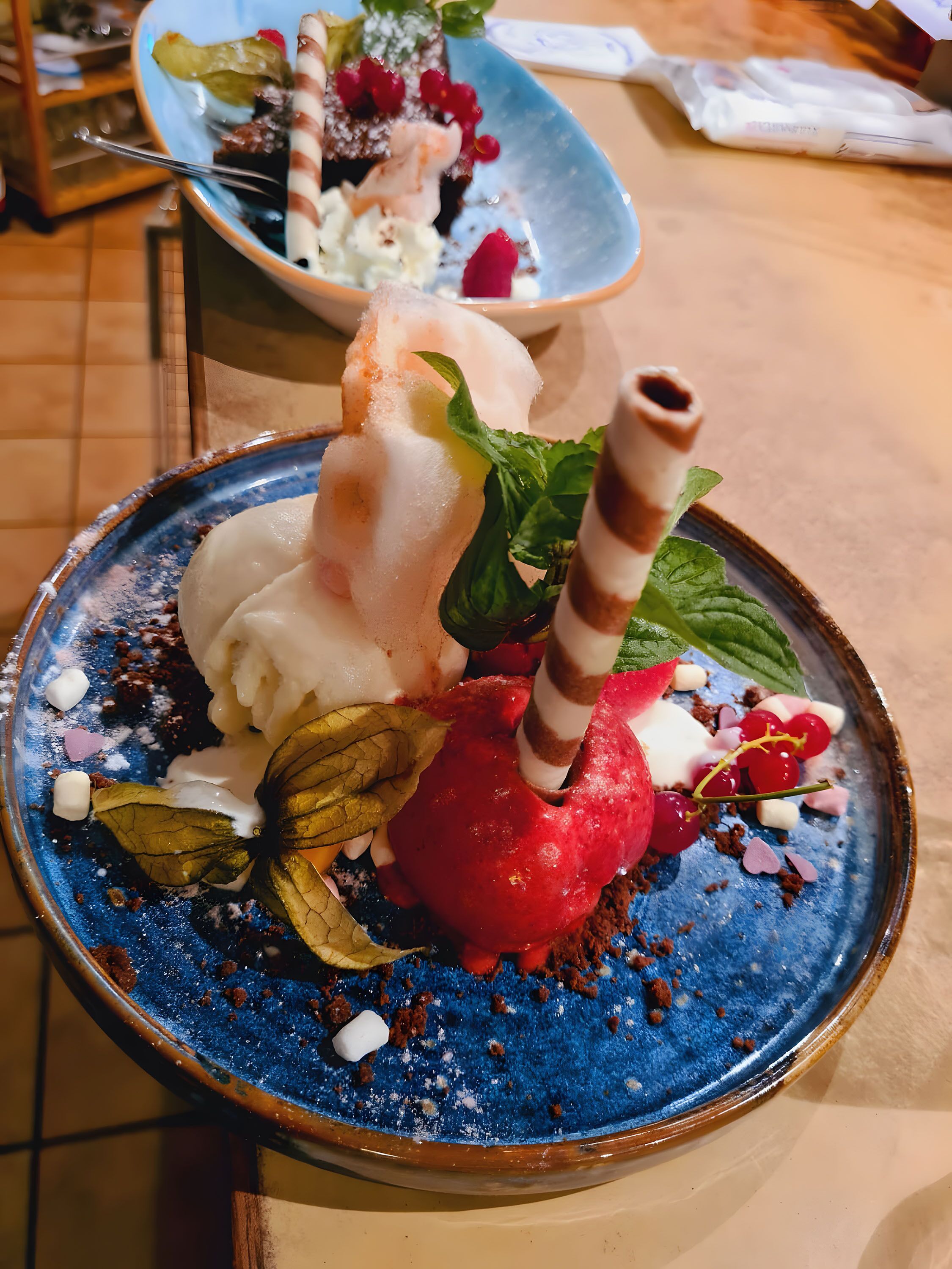 A dessert with ice cream, berries, mint, and chocolate on a blue plate.