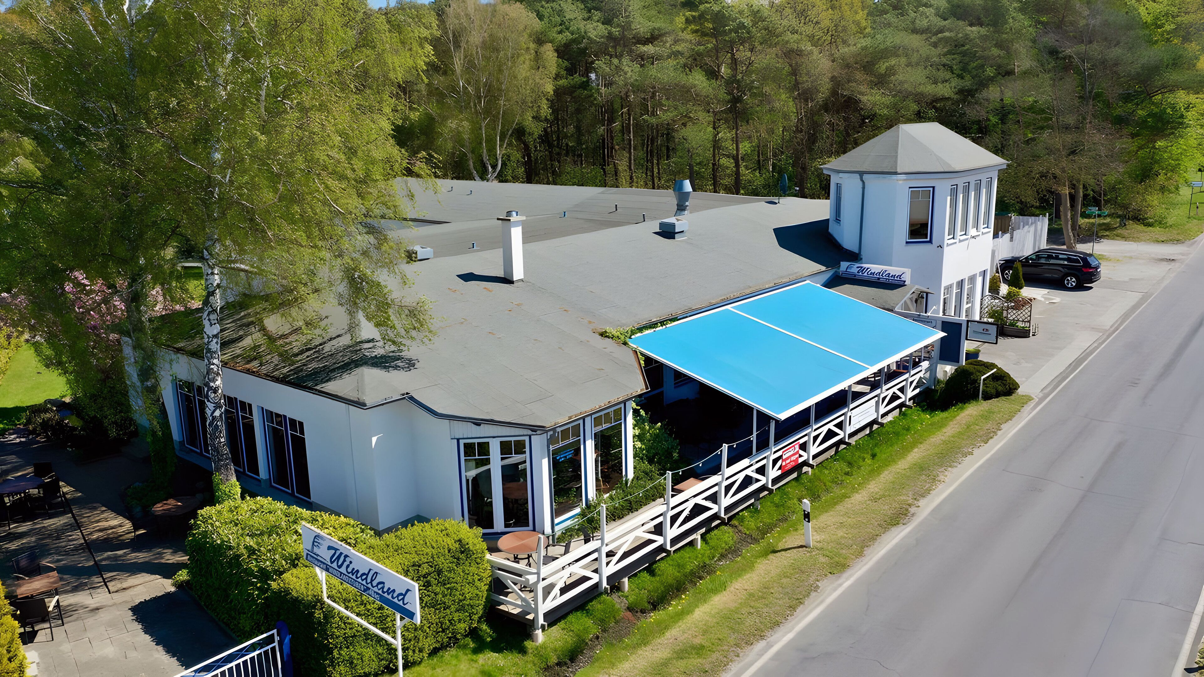 A building with a blue roof, a covered outdoor seating area, and a sign that reads "Windland."