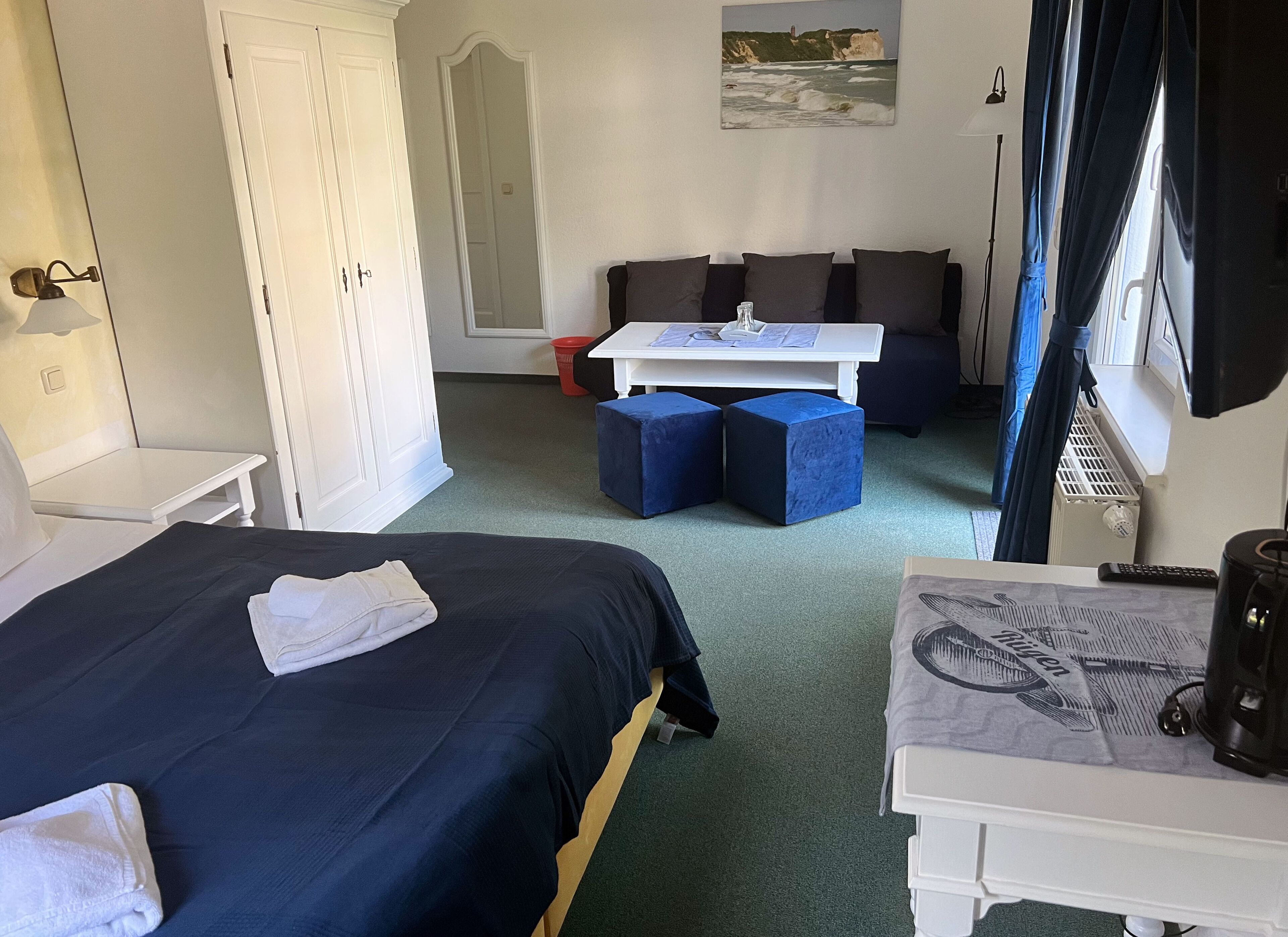 A hotel room with a bed, a desk, a chair, a sofa, and a window with curtains.