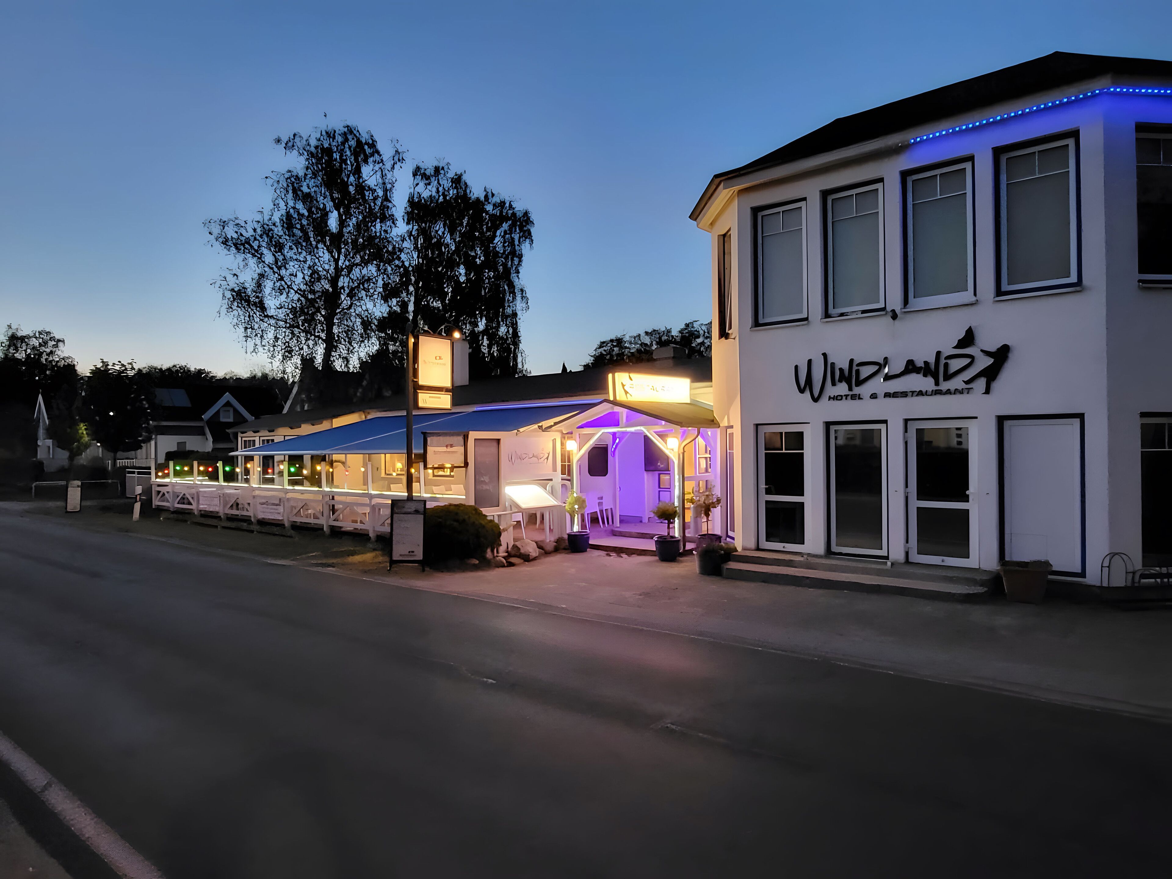A hotel with a sign reading "Windland Hotel & Restaurant" and a covered outdoor seating area with purple lighting.