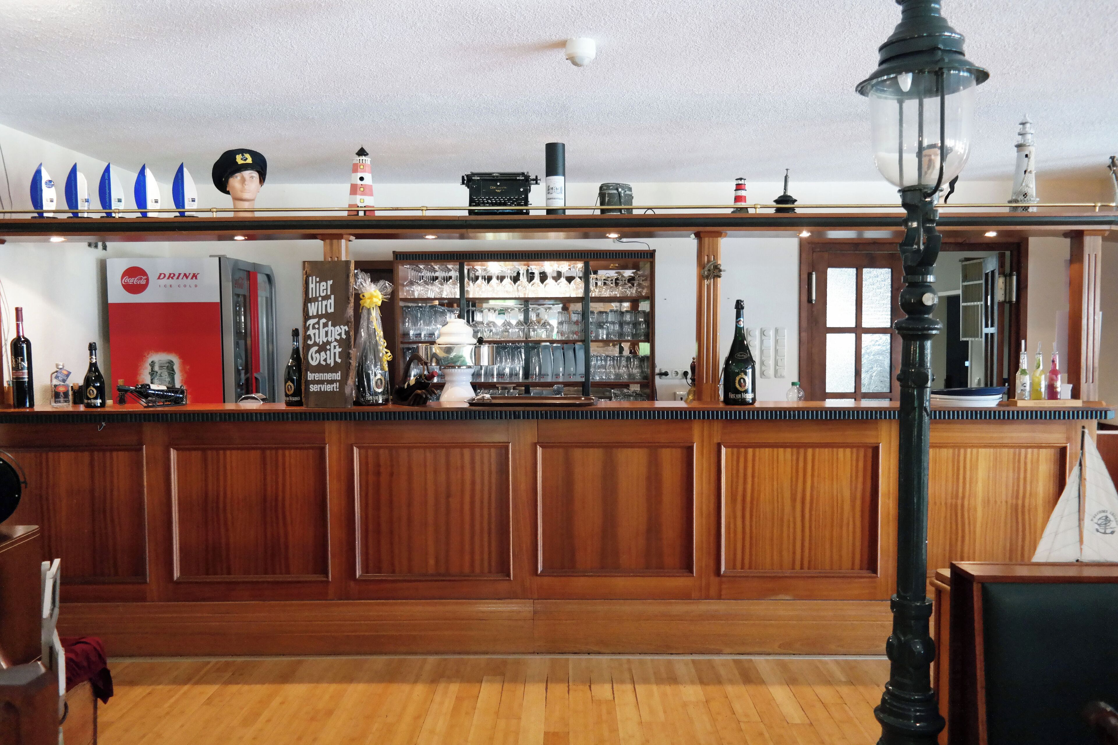 Eine Bar mit Holzwandverkleidung, einem Coca-Cola-Kühlschrank und einer Auswahl an Flaschen und Gläsern.