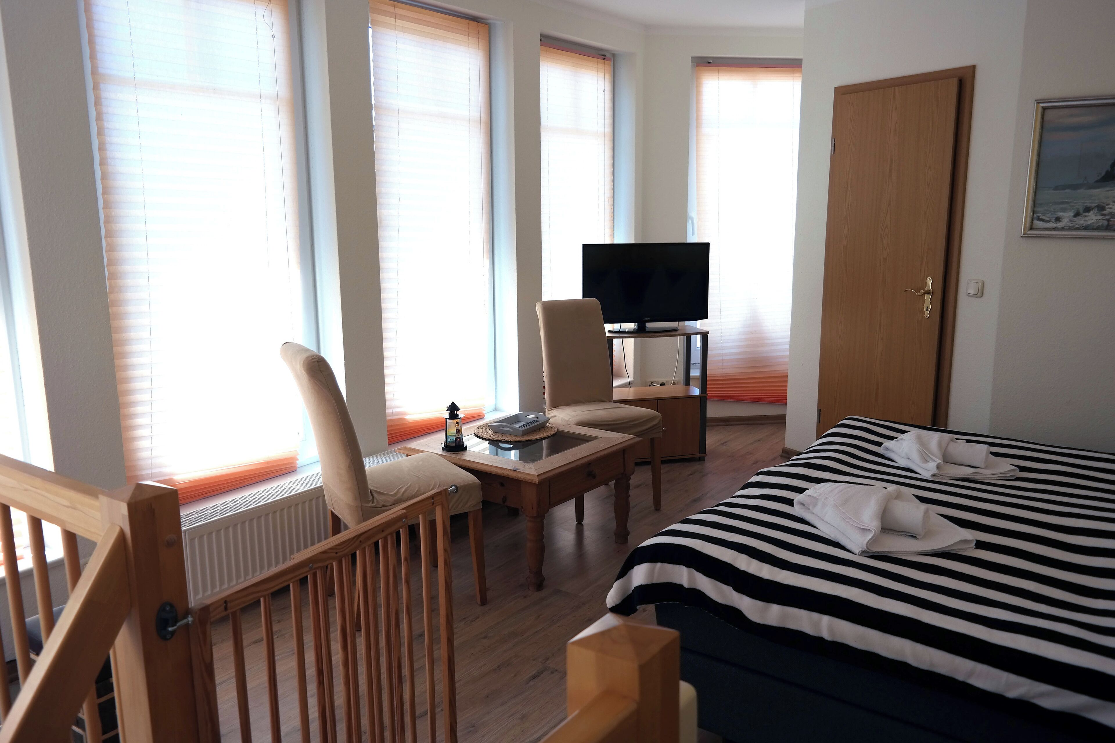 A hotel room with a bed, a desk with a chair, a television, and a window with blinds.