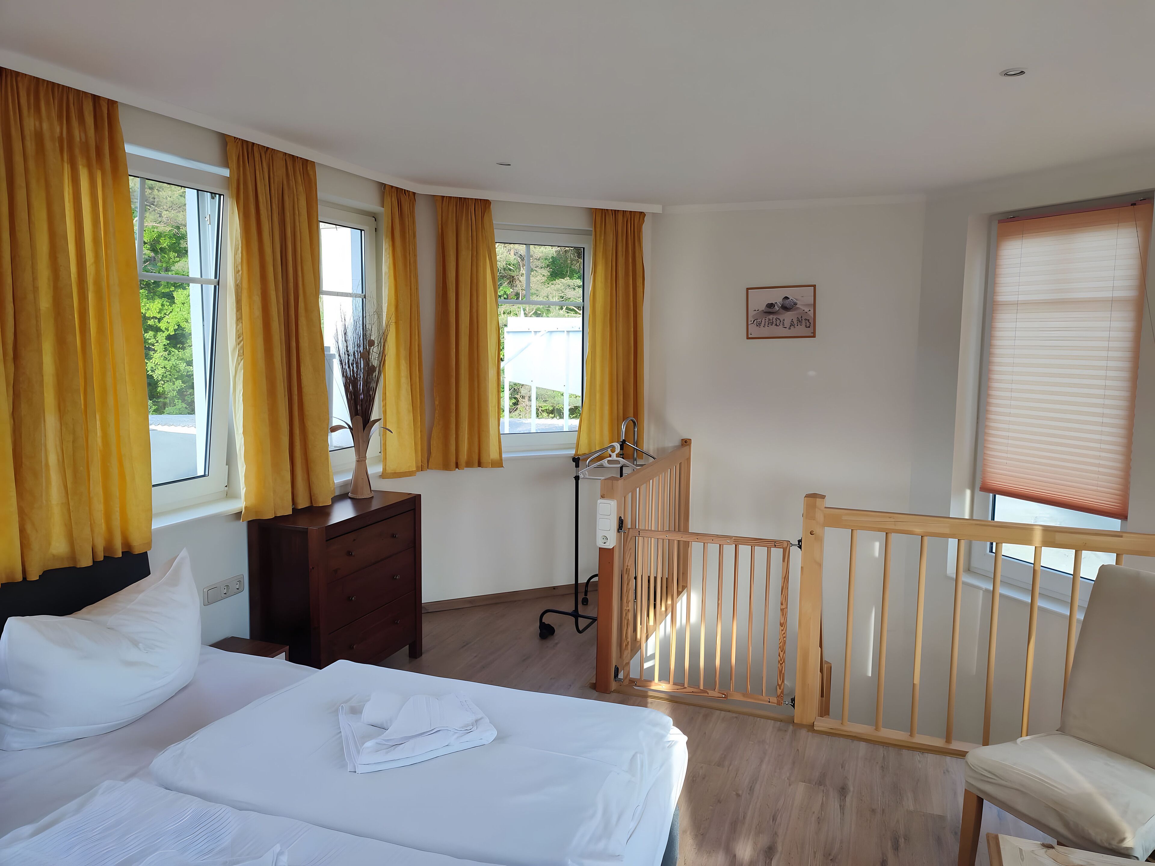 A bedroom with a bed, a wooden crib, a dresser, and a window with curtains.
