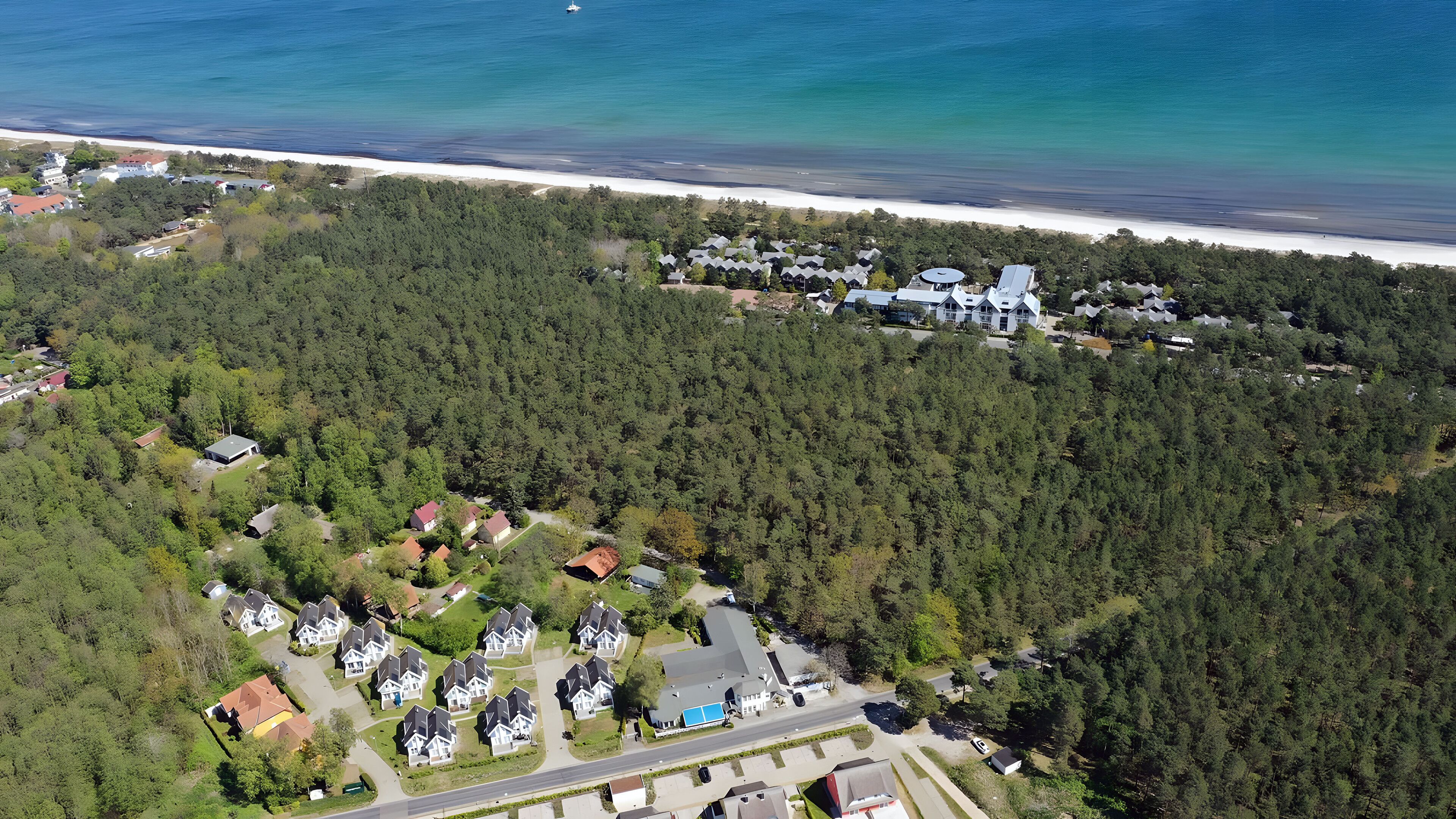 Eine Luftaufnahme eines Wohngebiets mit Häusern, einer Straße und einem Strand im Hintergrund.