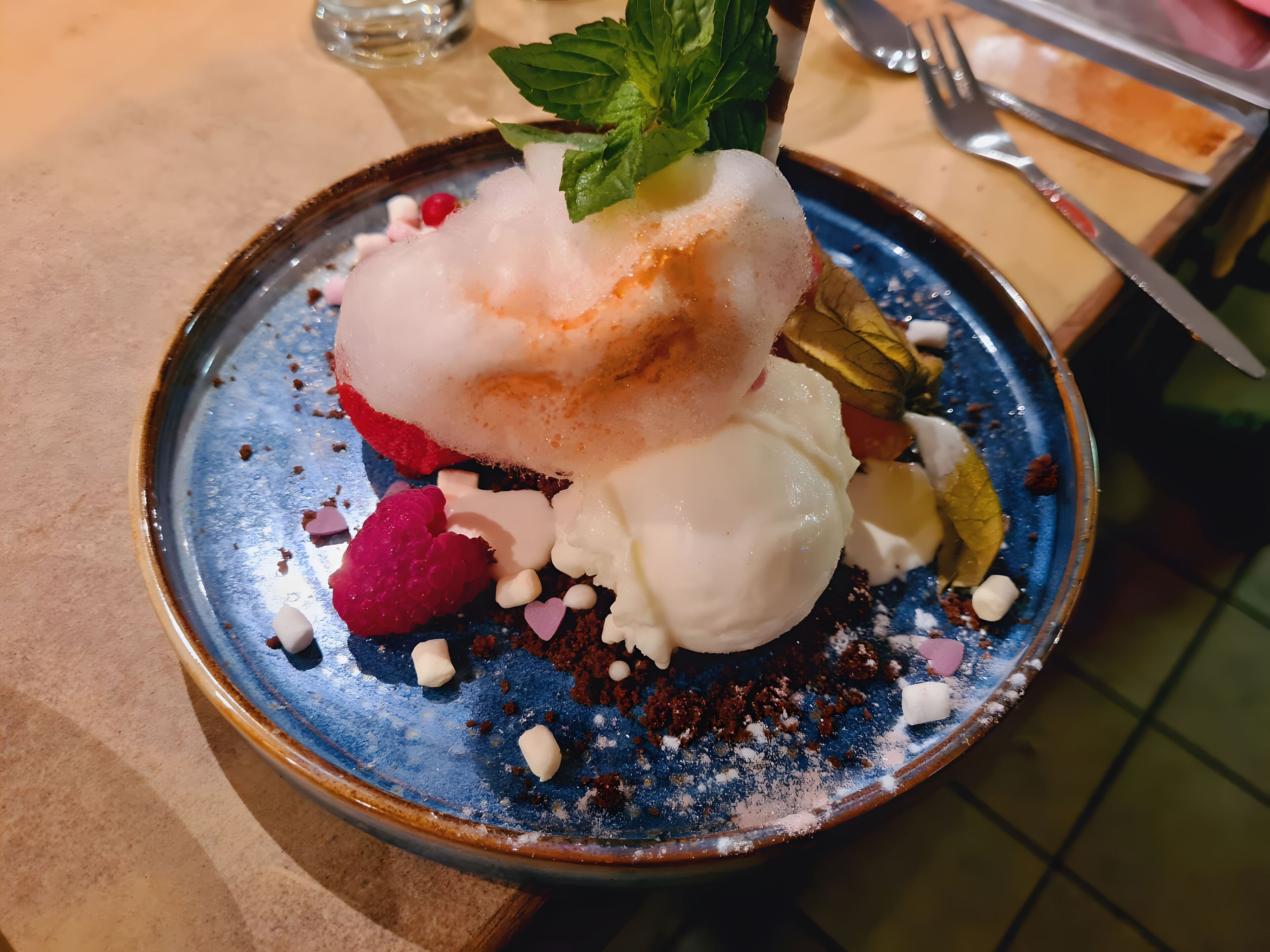 Un piattino con gelato, frutti di bosco e una foglia di menta su un vassoio di ceramica.