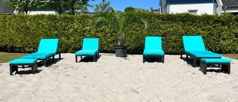 A sandy beach area with four turquoise lounge chairs arranged in a row.