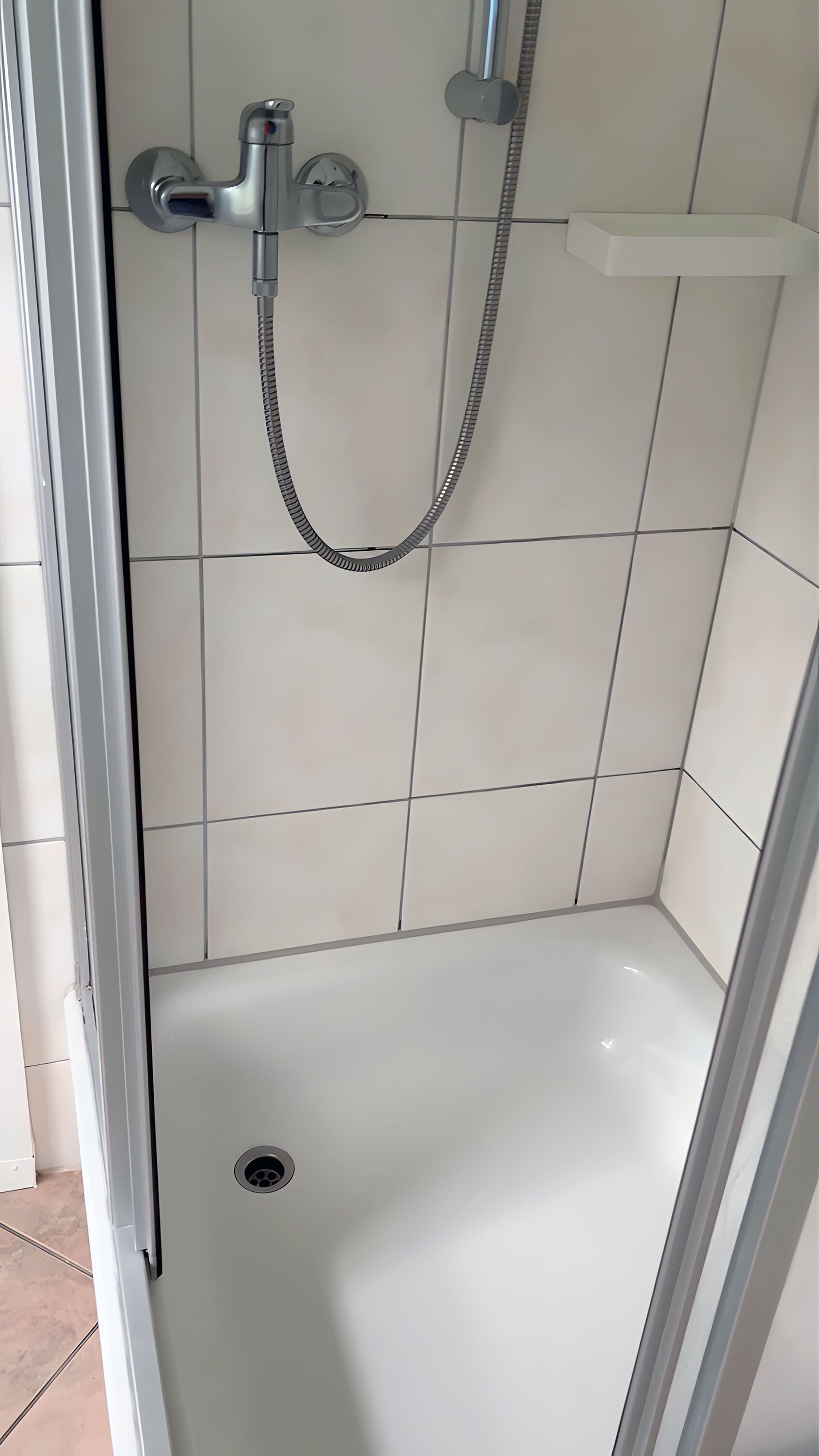 A shower with a handheld showerhead and a wall-mounted faucet.